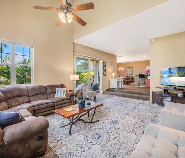 A spacious living room with a sectional sofa, TV, ceiling fan, rug, and view into the dining area, filled with natural light and decor.