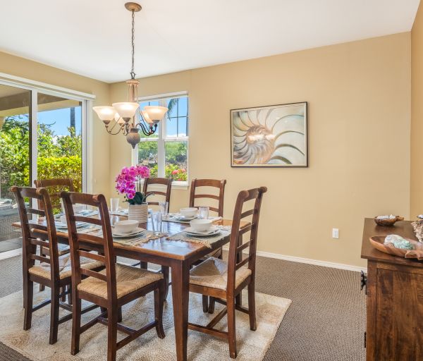 A dining room with a table set for six, featuring wooden chairs, a chandelier, artwork, and a view of a garden through glass doors.