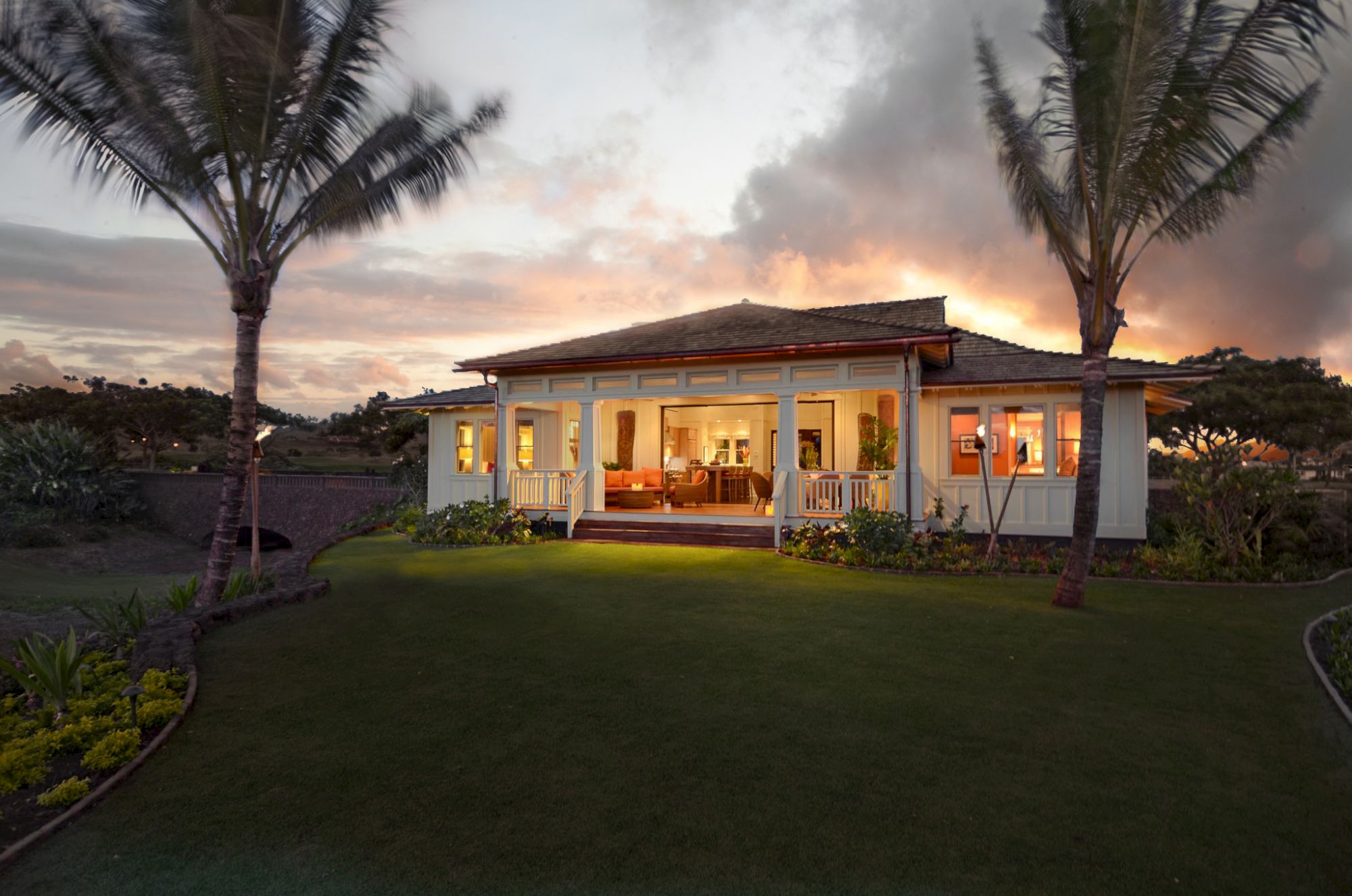 A beautifully designed house surrounded by lush greenery, with a sunset backdrop highlighting its inviting features.