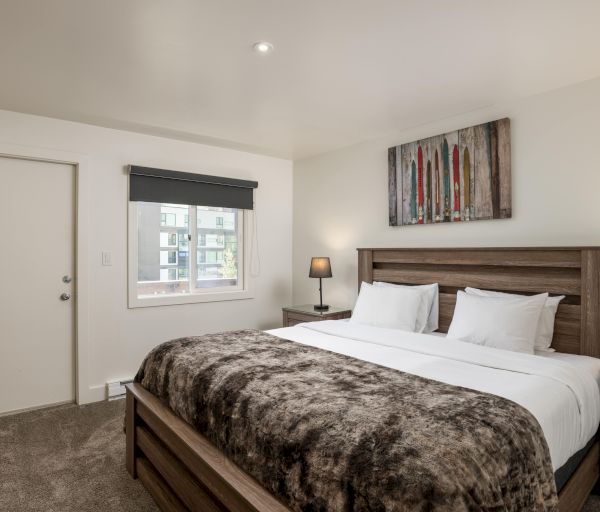 The image shows a cozy bedroom with a large bed, paintings, lamps, and a window showcasing an exterior view.