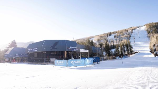 A ski resort with buildings, a snow-covered slope, and ski lift. Sunny weather and clear surroundings create a scenic winter scene.