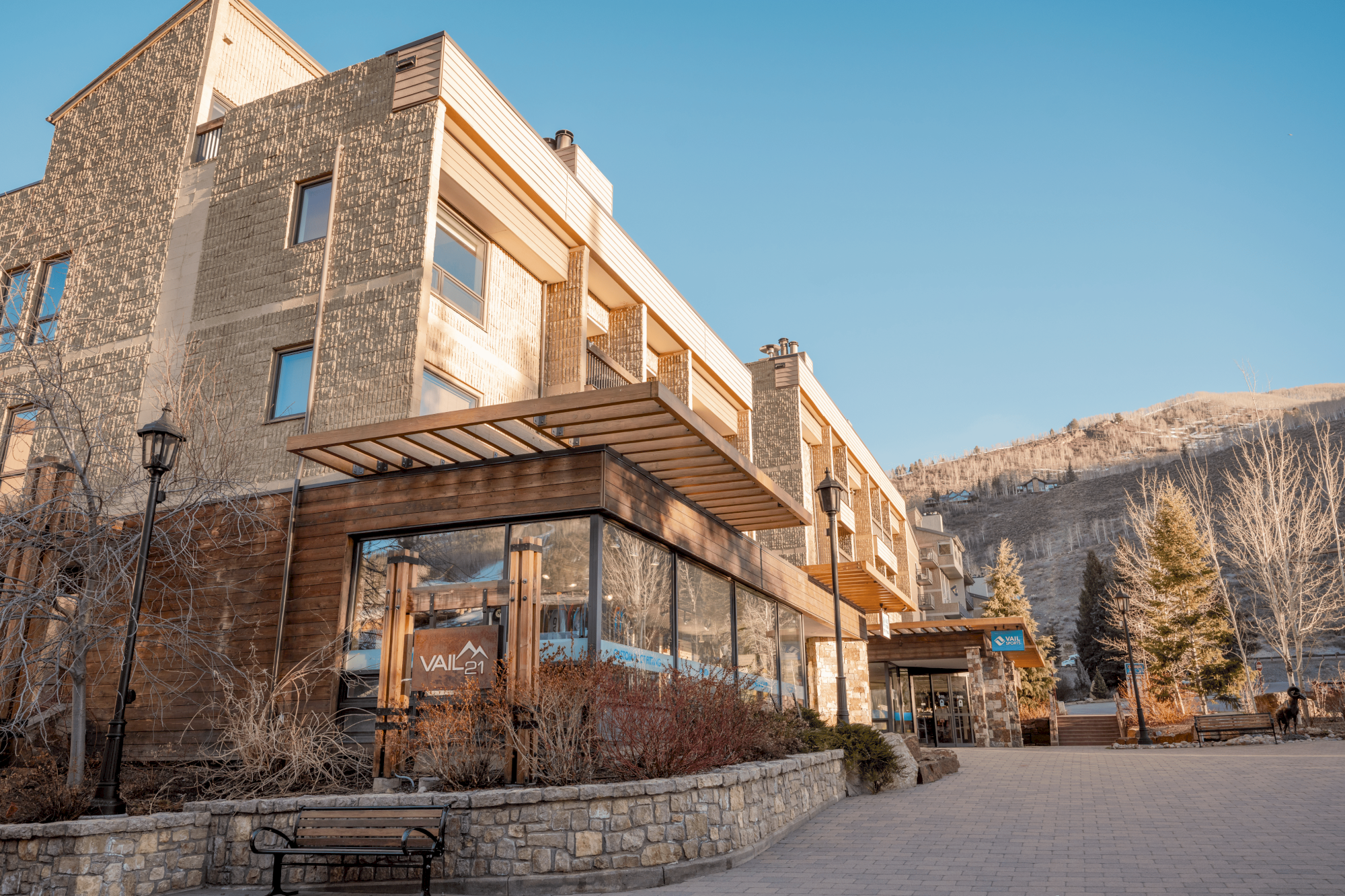 A modern building with large windows and wooden accents, set against a mountainous backdrop, under a clear blue sky.
