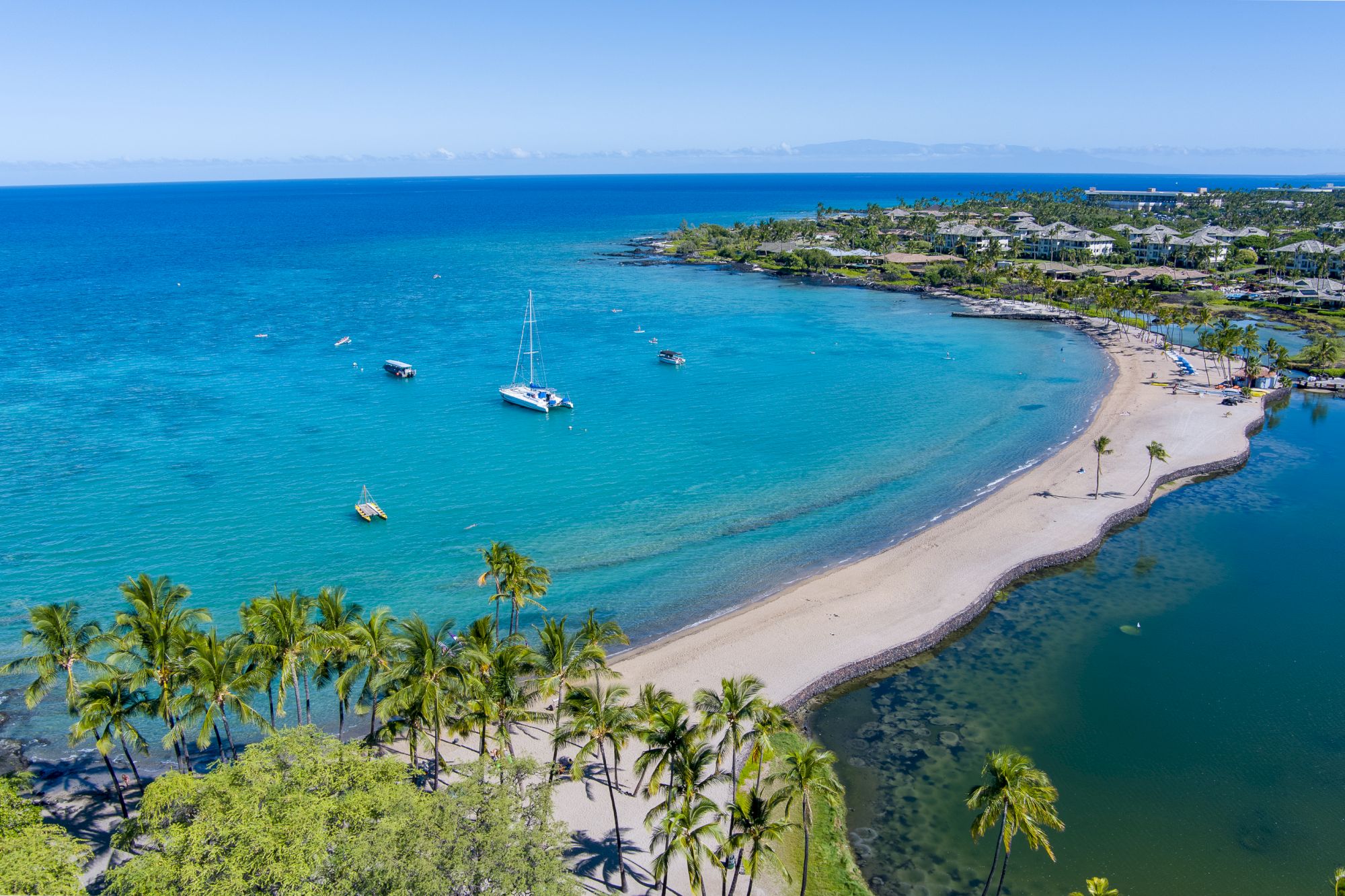 The image shows a beautiful tropical beach with clear blue waters, palm trees, boats, and a scenic coastline.