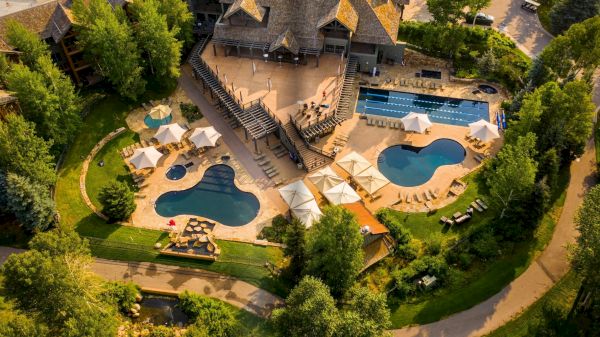 An aerial view of a resort with a large pool complex, winding lazy river, tanning decks, and surrounded by lush trees and stone buildings.