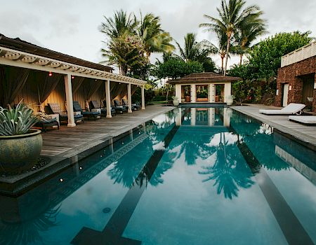 The image features a serene pool area with lounge chairs, palm trees, and a cozy gazebo, perfect for relaxation.