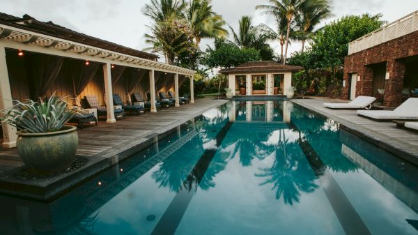 The image features a serene pool area with lounge chairs, lush greenery, and a cozy gazebo, reflecting a tranquil vibe.