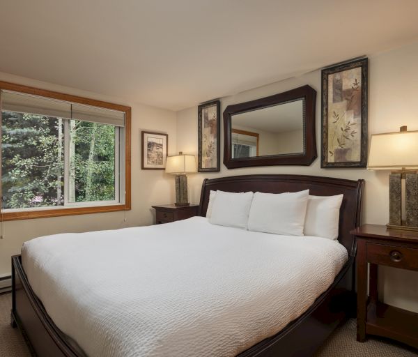 The image shows a cozy bedroom with a large bed, bedside table, lamp, and window overlooking greenery. It's inviting and serene.