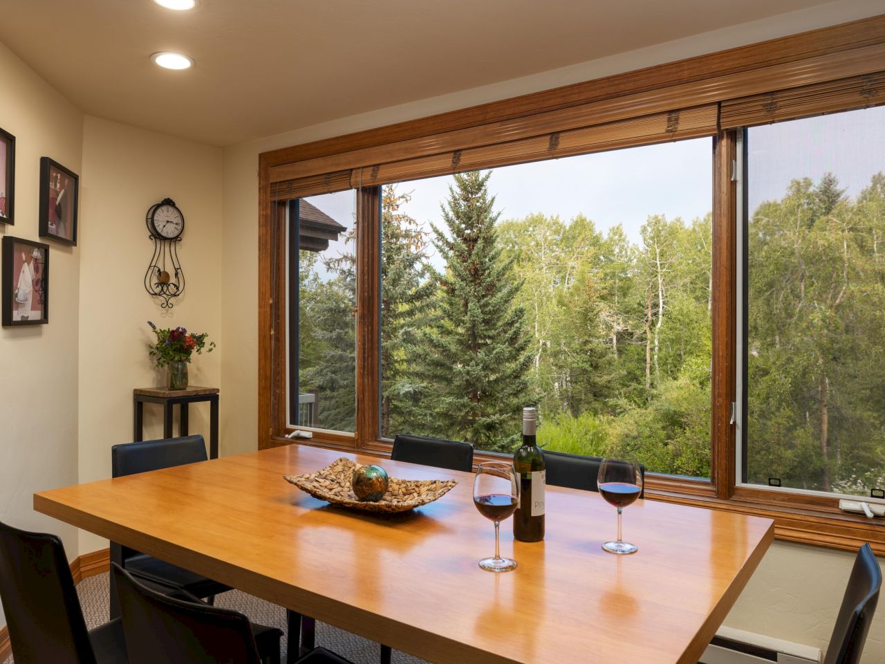 The image showcases a dining area with a wooden table, wine glasses, and a view of trees outside, creating a cozy ambiance.