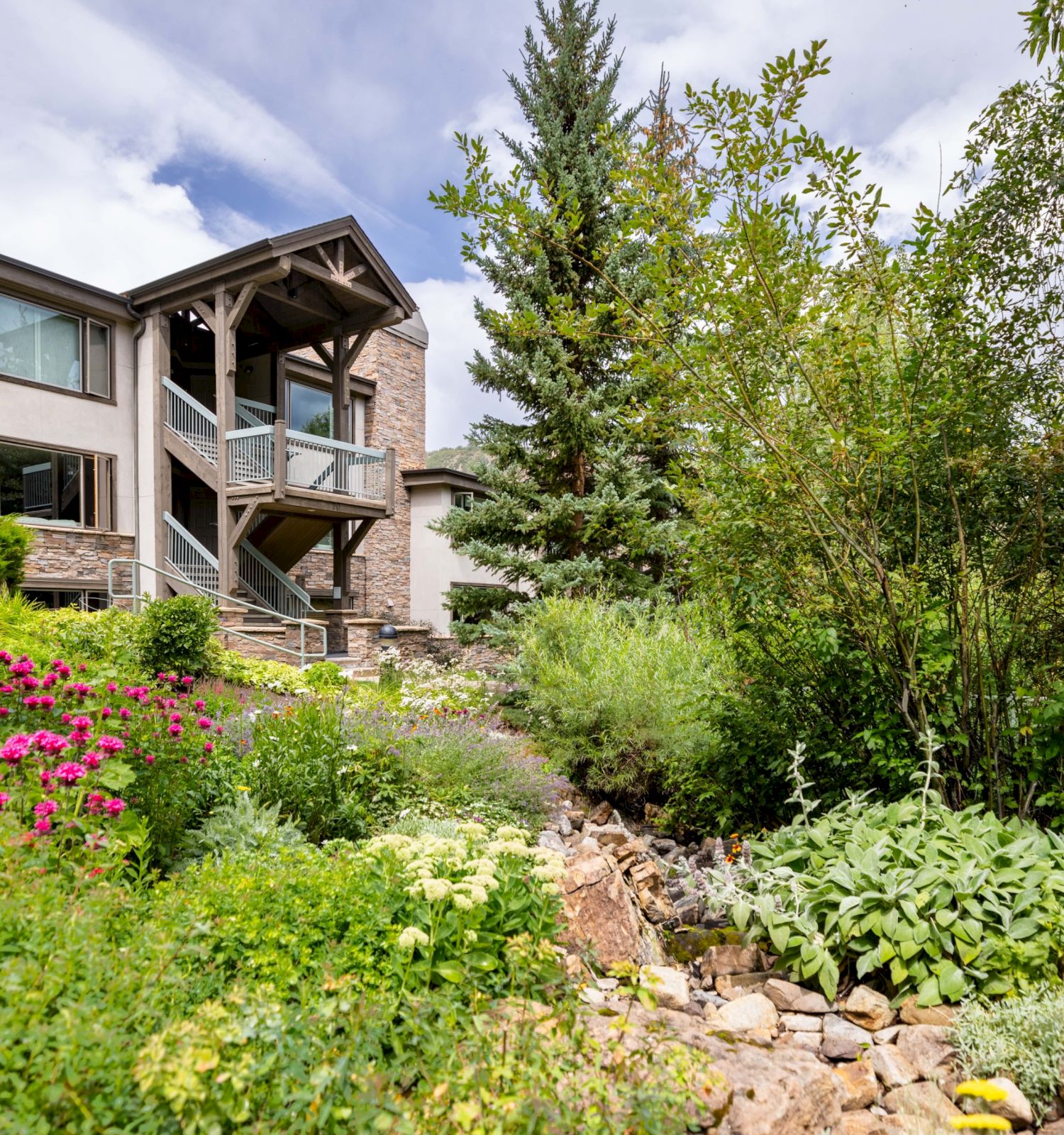 The image shows a multi-level building surrounded by colorful gardens and lush greenery, with a peaceful atmosphere and clear skies.