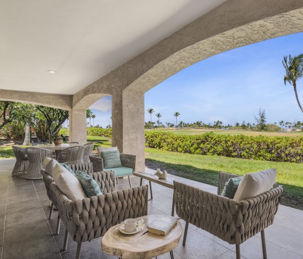 A serene patio with woven chairs, a wooden table, and lush greenery in view, creating a peaceful outdoor space.