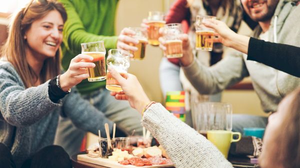 A group of friends cheers with drinks, enjoying a lively gathering around a table with snacks. Good times are being shared.