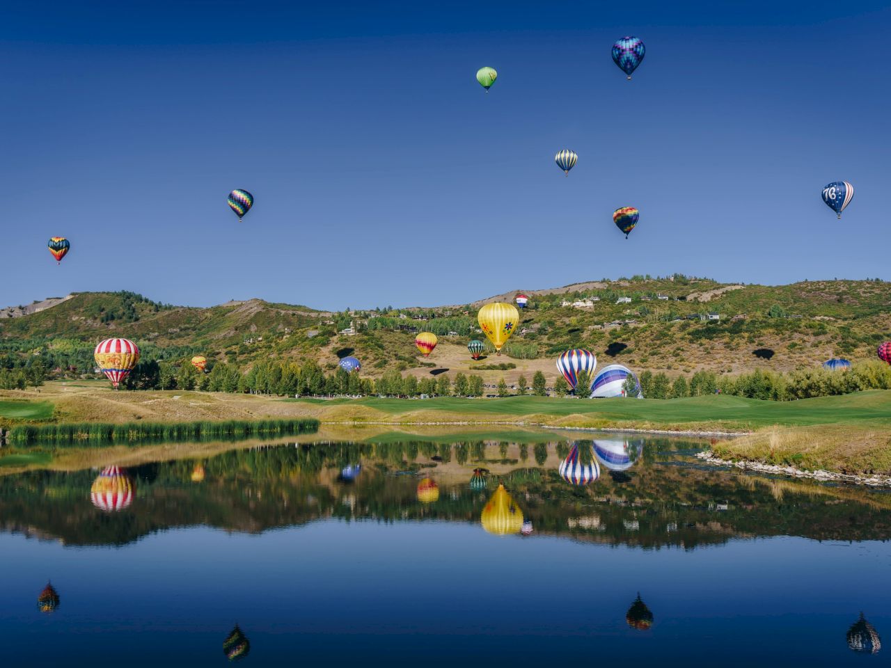 The image features numerous hot air balloons floating over a serene landscape, with reflections visible in a calm body of water.