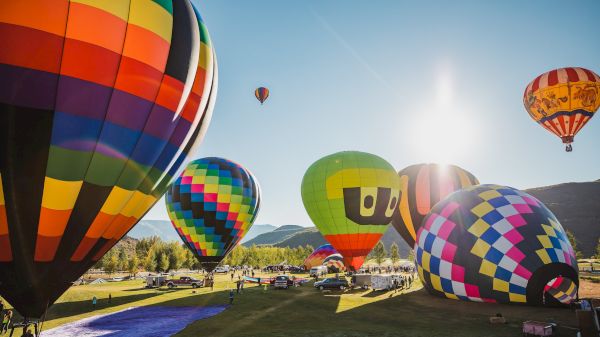 The image features colorful hot air balloons at a festival, with blue skies and a bright sun illuminating the scene.