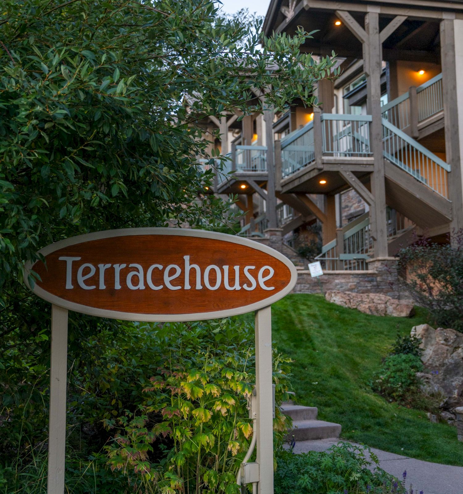 The image features a sign for "Terracehouse" near a multi-level building surrounded by greenery and illuminated by warm lights.