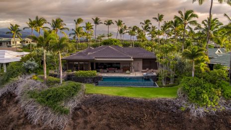 The image features a luxurious house with a pool, surrounded by lush palm trees and greenery, set against a cloudy sky backdrop.