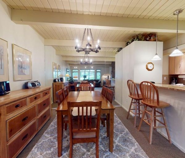The image shows a cozy dining area with a wooden table, chairs, and a connected kitchen featuring modern appliances.