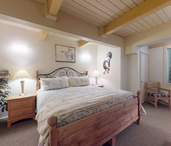 The image shows a cozy bedroom with a wooden bed, nightstand, lamp, and a decorative wall piece, creating a warm atmosphere.