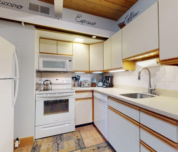 The image shows a modern kitchen with white appliances, wooden accents, and a clean countertop setup, ideal for cooking.