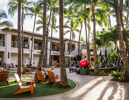 A sunny hotel courtyard with palm trees, lounge chairs, and a central circular area; people relax by the poolside.