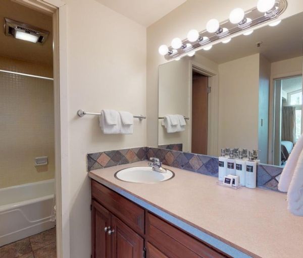 The image shows a clean bathroom with a sink, mirror, towels, and a shower area, featuring a bright light fixture above.