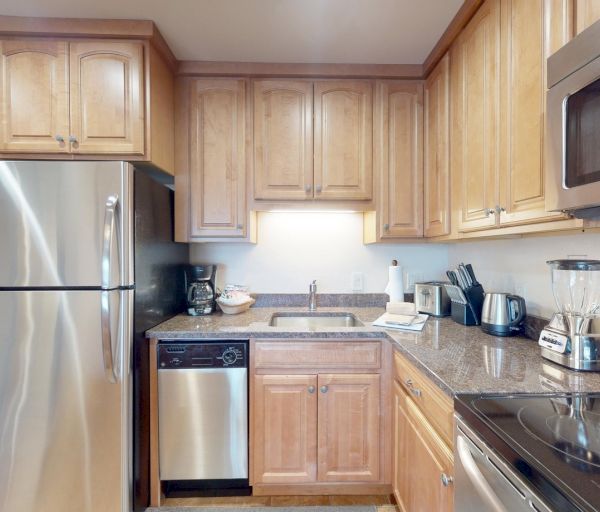 The image shows a modern kitchen with wooden cabinets, stainless steel appliances, and granite countertops for a sleek look.