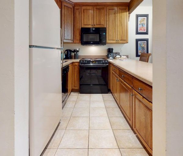 The image shows a kitchen with wooden cabinets, a stove, a refrigerator, and tiled flooring, creating a cozy cooking space.