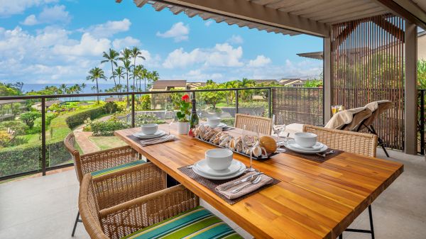The image shows a beautiful outdoor dining area with a wooden table, dishes set, and a stunning ocean view filled with greenery.