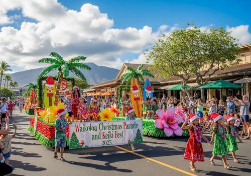 A festive parade on a sunny street with colorful floats, tropical palm props, dancers in bright skirts, and a banner reading &ldquo;Wailoa Christmas Parade and Keki Fest&rdquo; amid cheering crowds.