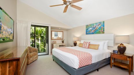 A bright, inviting hotel-style bedroom with a king bed, ceiling fan, and balcony access. (140 characters max, ends with a period.)