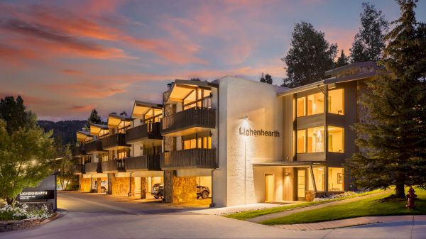 The image shows a modern building called Lichenhearth, surrounded by trees and a beautiful sunset sky, creating a serene atmosphere.