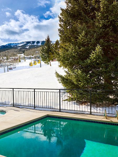 The image shows a snowy landscape with a pool, mountains in the background, and ski lifts, creating a serene winter scene.