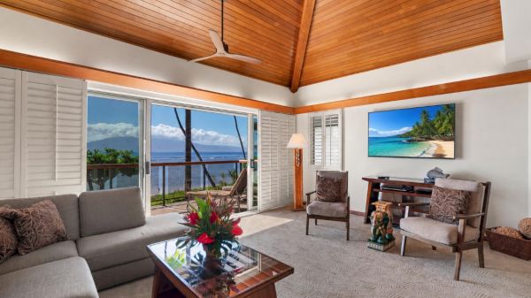 A bright tropical living room with a ceiling fan and balcony view of the ocean, stylish seating, and a flat-screen TV.