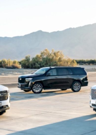 Three modern SUVs parked on a tarmac with mountains in the background, sunlight glow, white and dark-colored vehicles facing different directions.