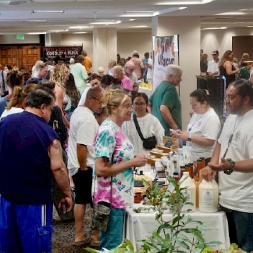Crowd at a busy indoor market or expo tasting booths, people chatting, sampling foods and drinks, vendors behind tables.