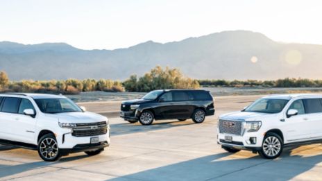 Three modern SUVs parked on a sunny runway or open lot, with mountains in the background and a lens flare.