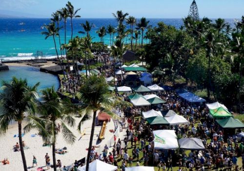 Beach, palm trees, and a crowded shoreline with umbrellas and people; ocean in the background.