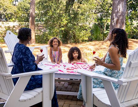 Four people sitting around a white table outdoors, sharing drinks and snacks in a sunny garden setting.