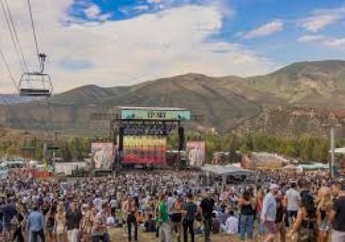 A large outdoor music festival with a stage, crowd, and mountains in the background, plus a gondola lift in the sky.