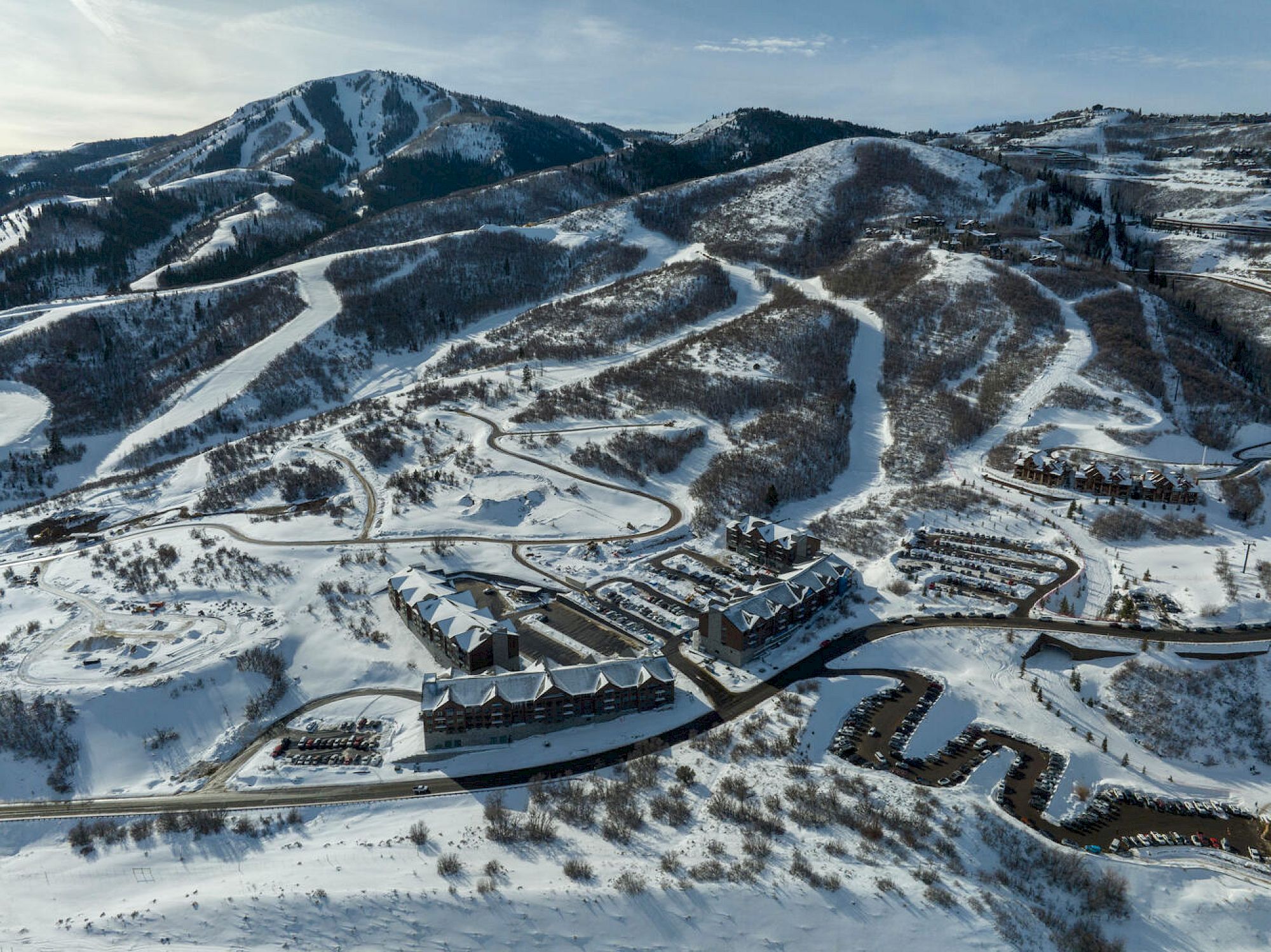 Snow-covered mountains with winding roads, compact buildings, and a fortress-like complex nestled in the valley.