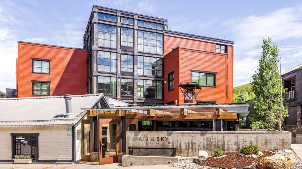 A modern, multi-story building with red-orange panels, large glass windows, and a small outdoor seating area labeled "Main & Sky."