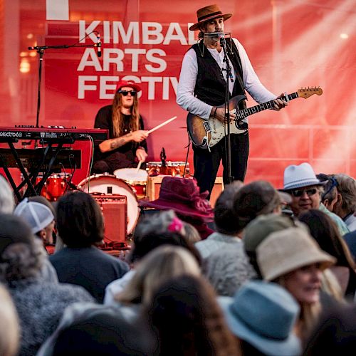 A live band performs on stage at Kimball Arts Festival, with a guitarist and drummer in front of a cheering crowd.
