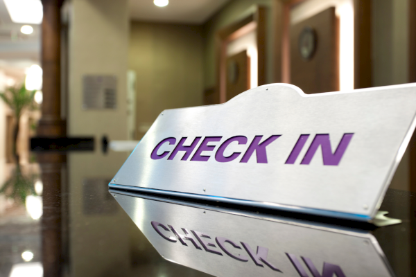 Hotel check-in sign on a reception desk in a dim lobby, glossy surface, purple text says &ldquo;CHECK IN.&rdquo;