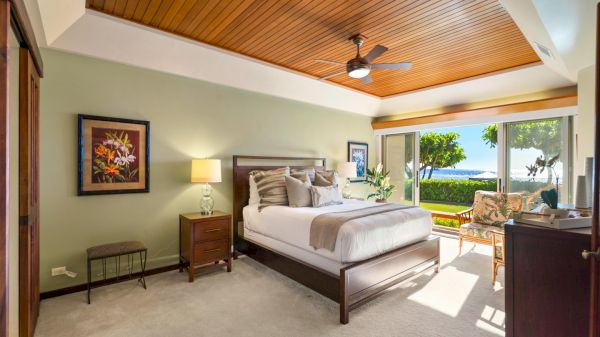 A luxurious bedroom suite with a wooden ceiling, large bed, sitting area, and access to a sunny outdoor view overall.