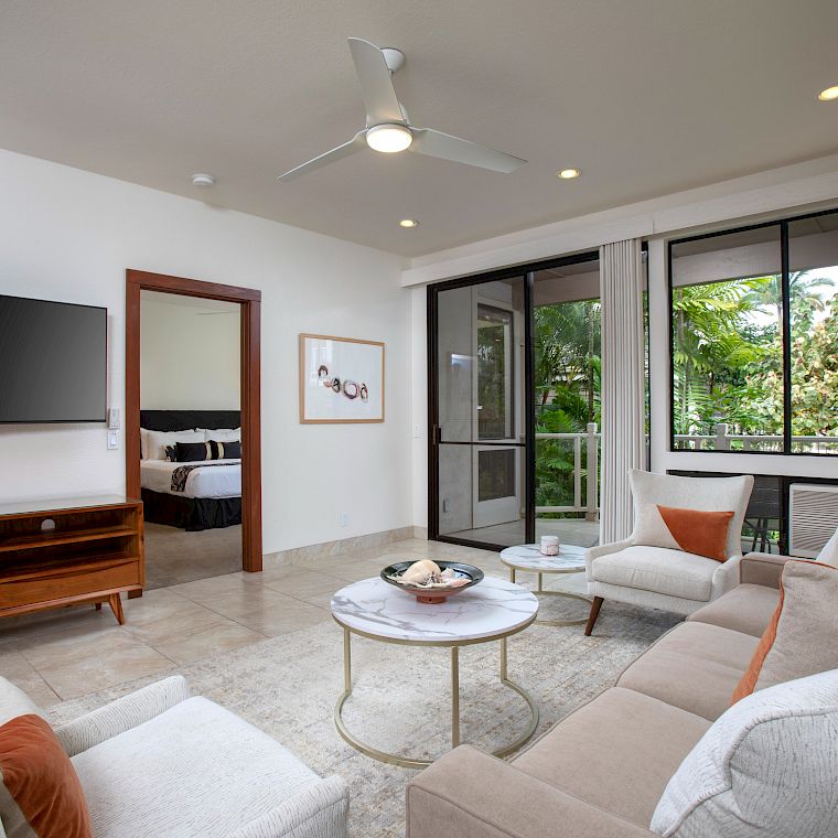 Cozy modern living room with beige and white furniture, wall-mounted TV, a round coffee table, orange accents, and large windows with a balcony view.