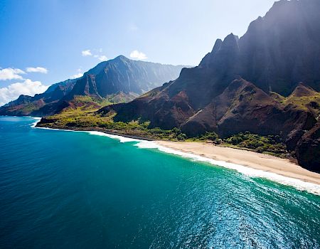 A breathtaking tropical coastline with turquoise water, a sandy beach, and dramatic jagged mountains looming over the shore.