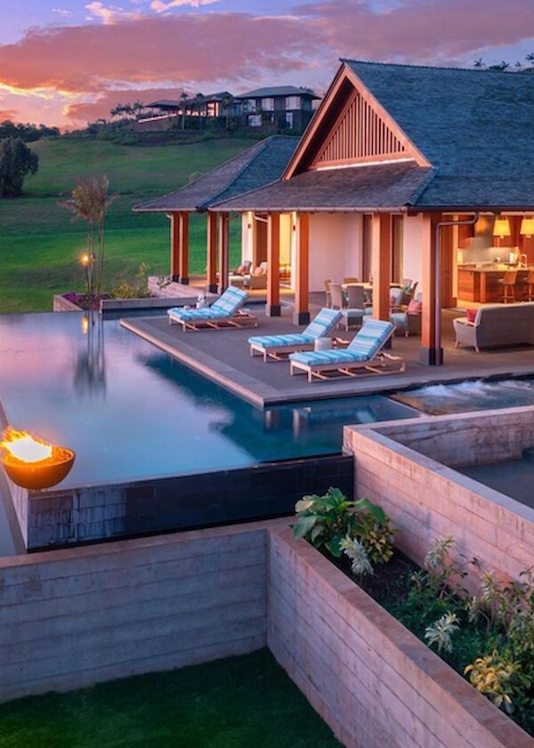 A luxurious hillside villa with an infinity pool, warm lighting, and sunset views over green fields and rolling landscape.