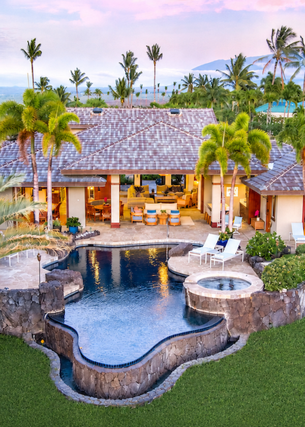 Luxurious tropical villa with a freeform pool, hot tub, palm trees, and lush landscaping overlooking a serene backyard retreat.