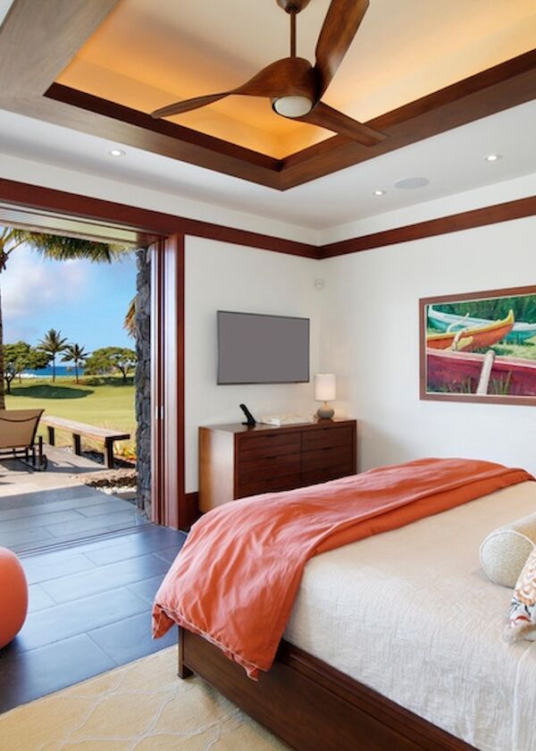 A stylish tropical hotel room with a large bed, orange accents, and a glass door opening to an outdoor patio and beachside view.