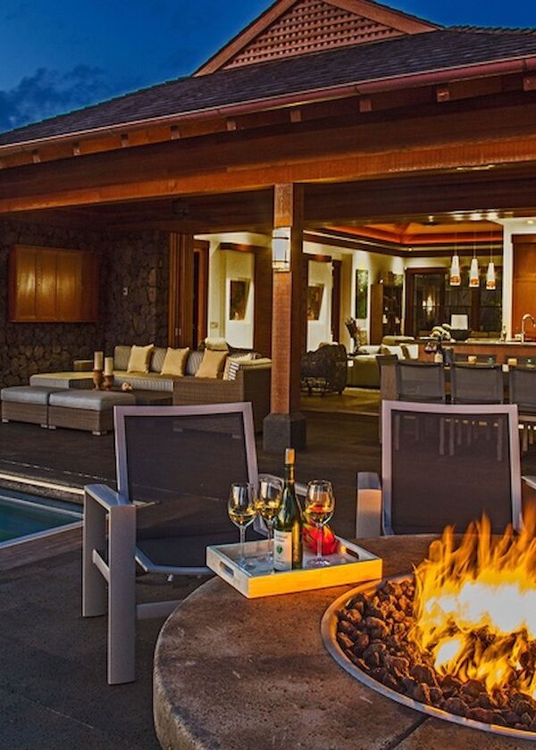 A luxurious outdoor lounge by a modern house with a pool, cozy fire pit, and stylish seating under a covered patio, evening vibe.