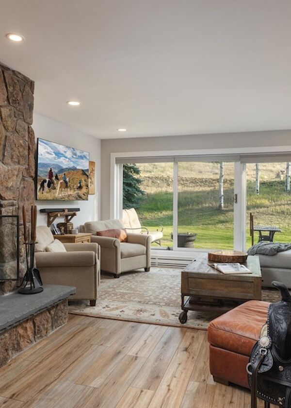 Cozy living room with a stone fireplace, large glass sliding doors, and a mix of tan and brown seating, plus a black riding horse statue near the foreground.